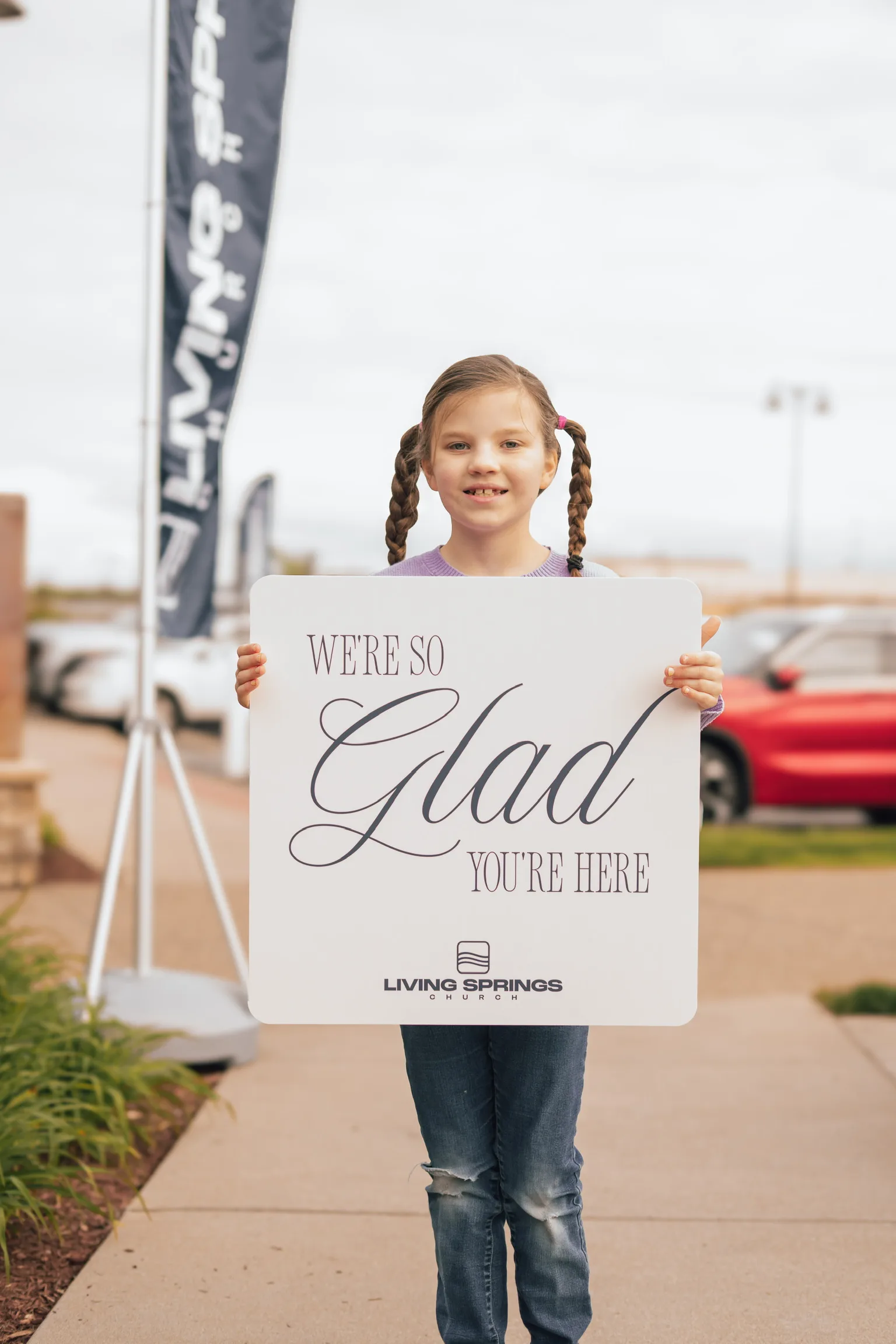 A young girl with braids holding a Glad You’re Here sign